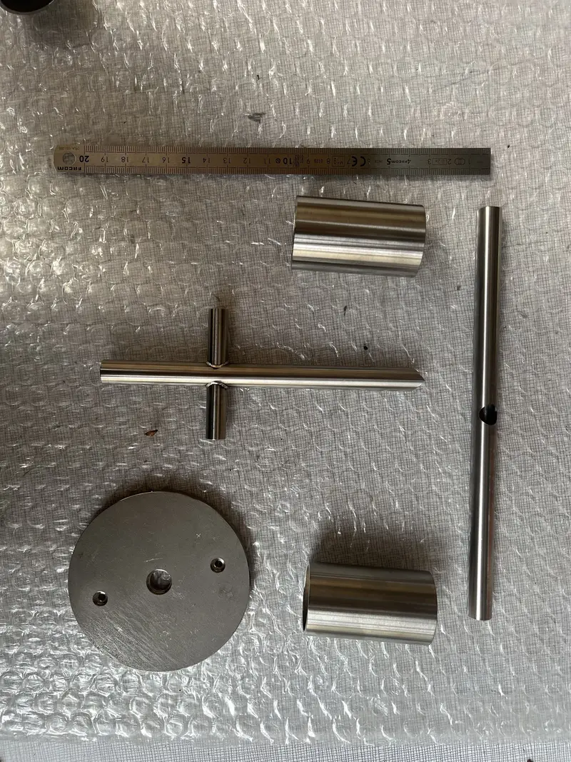 Pièces en inox usinées avant assemblage : tubes, croisillon soudé et platine, présentées au réglet